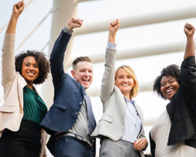 Four professionals smiling with their arms raised in the air