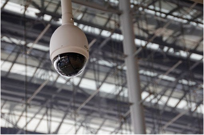 A white, oval camera hanging from ceiling beams