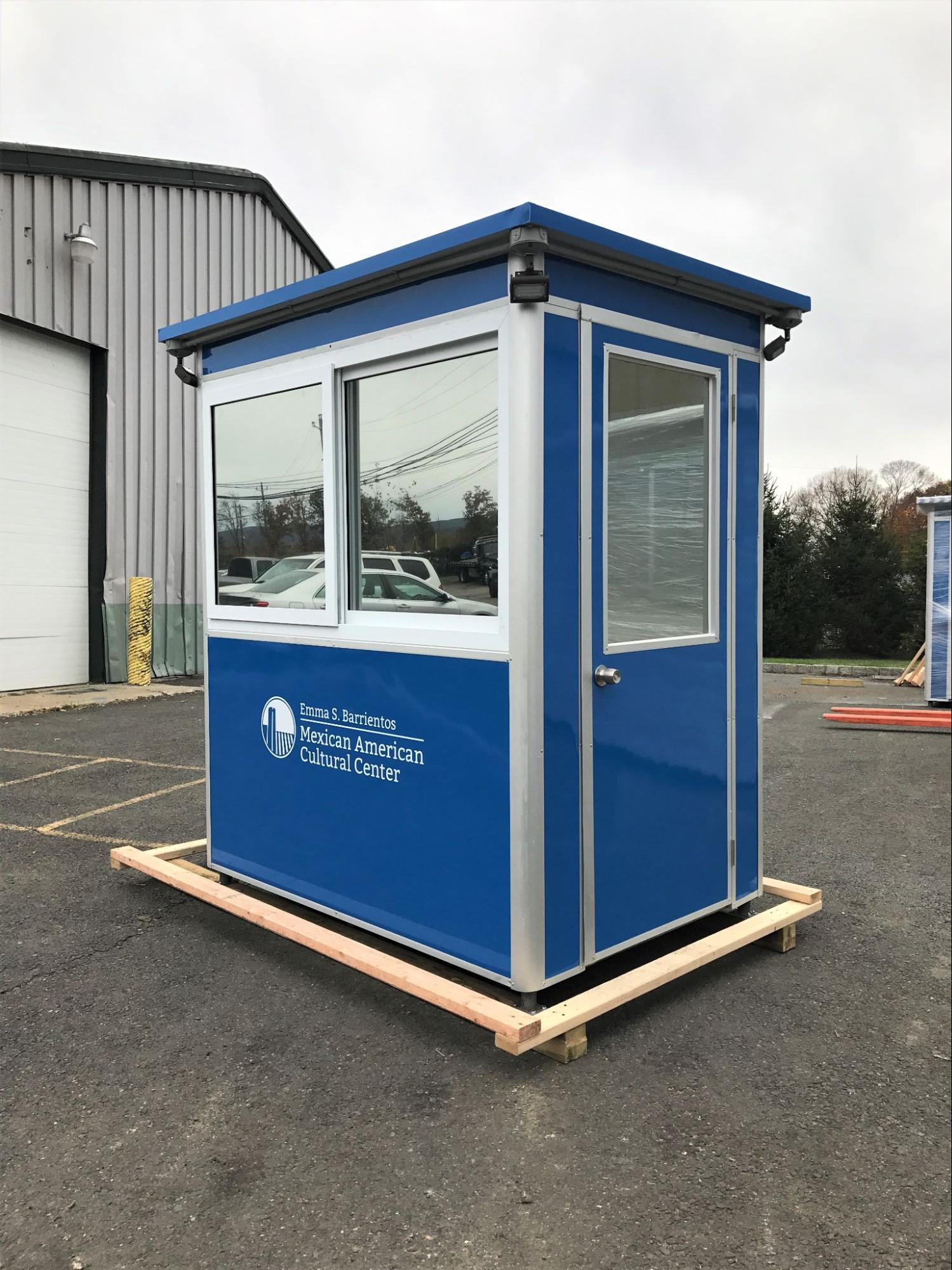 A blue prefab welcome center customer service booth advertising the Mexican American Cultural Center atop a platform