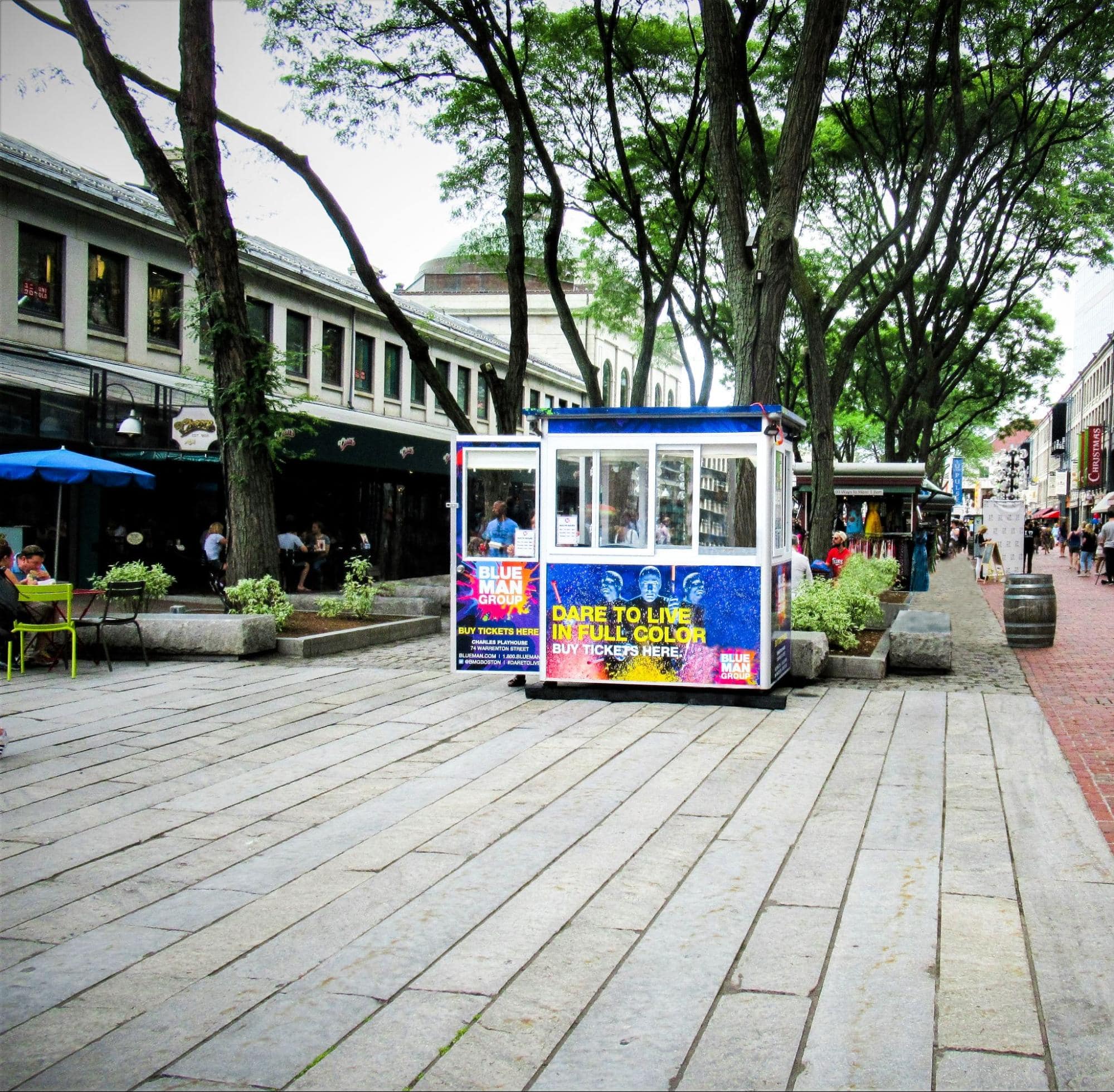 A blue premanufactured booth advertises an upcoming event to customers in a busy plaza