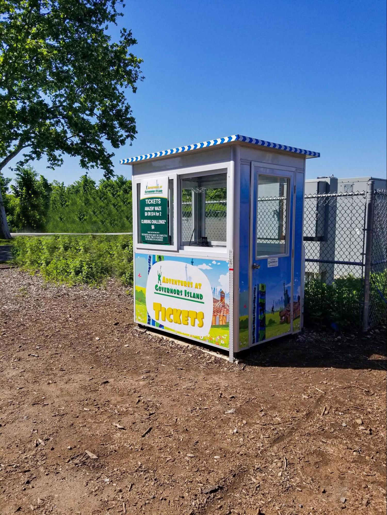 A modular structure in a wooded area features a ticket price banner, a customer service window, and brightly decorated walls