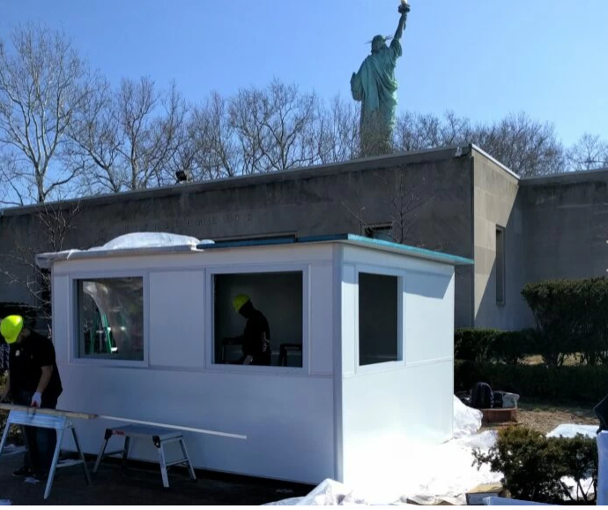 Workers assemble a white tourism prefab booth near the Statue of Liberty
